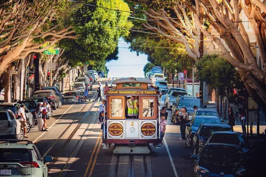 A 威尼斯人官网平台app cable car approaches on a tree-lined street.